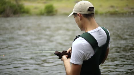 toma en cámara lenta de un pescador que usa vadeadores preparando su cebo y mosca mientras pesca con mosca