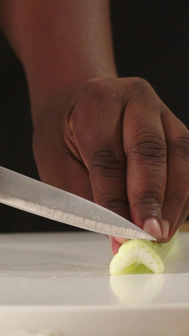 Vertical video: Placing round board, cook in khaki slicing celery with knife on counter for salad