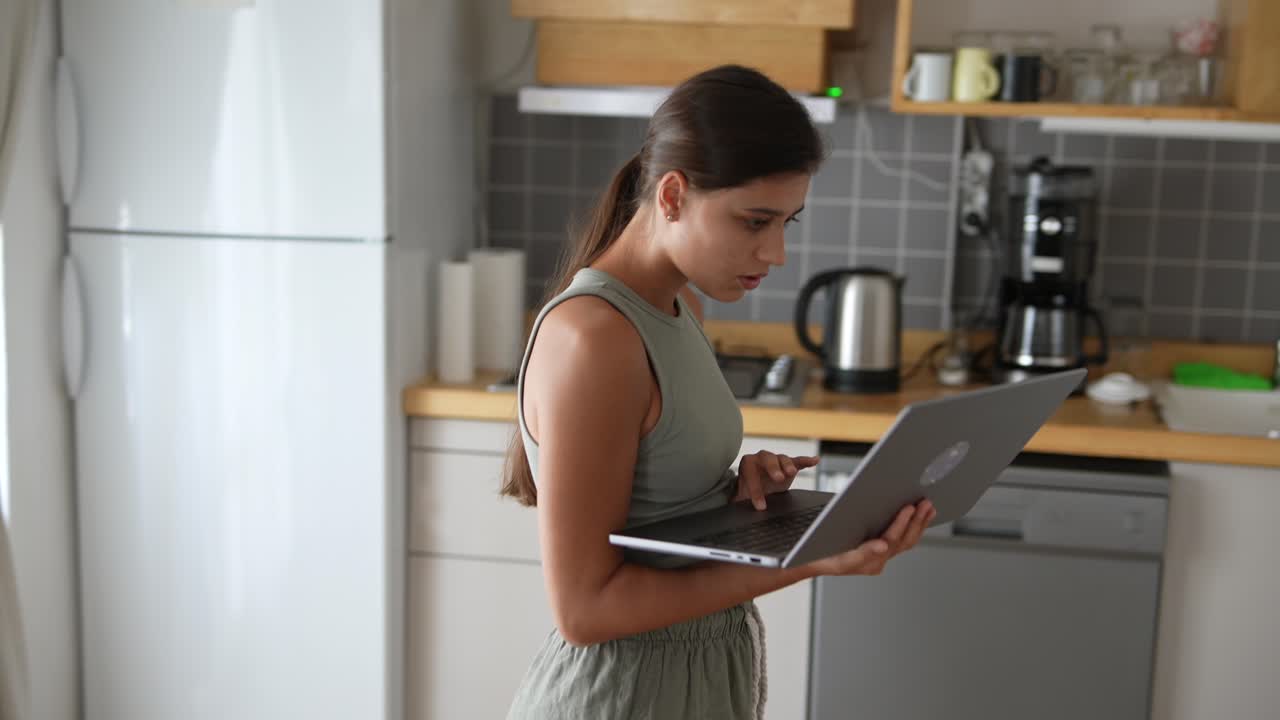 mujer joven trabajando en una computadora portátil en la cocina