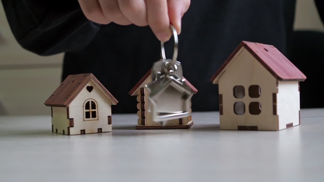 llavero con las llaves del nuevo apartamento en la mano. casas de juguete de madera contrachapada en la mesa. compra de bienes raíces