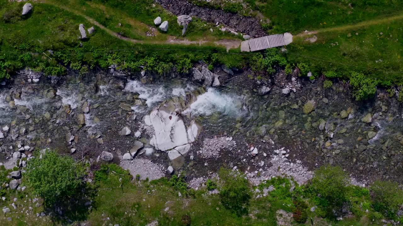 Crystal clear mountain stream passing under a small bridge with surrounding vegetation