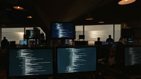 programmers working in a dark office with ocean view and code on screens