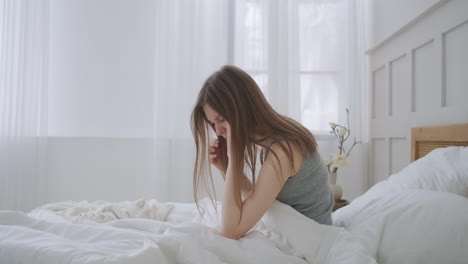 women sitting on bed holding her head. she has a painful headache. the woman experiences a headache rubs her temples and frowns in pain. seasonal disease caucasian girl in the bedroom on sick leave