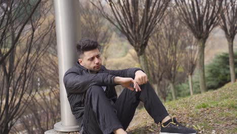 the young man leaning on the pole outdoors is depressed and thoughtful.