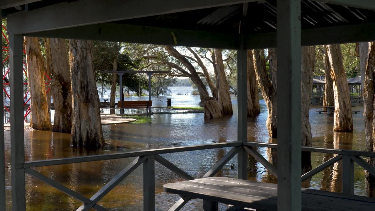 Slow motion landscape of lake overflow flooding water from storm into public community park with shelter pergola table and trees in playground of Budgewoi Central Coast Australia hazard weather risk