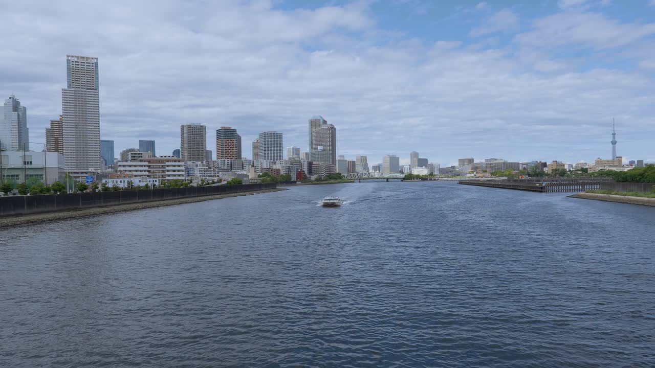 A peaceful shot of a passenger boat traveling down a river with the Tokyo cityscape and modern buildings in the background