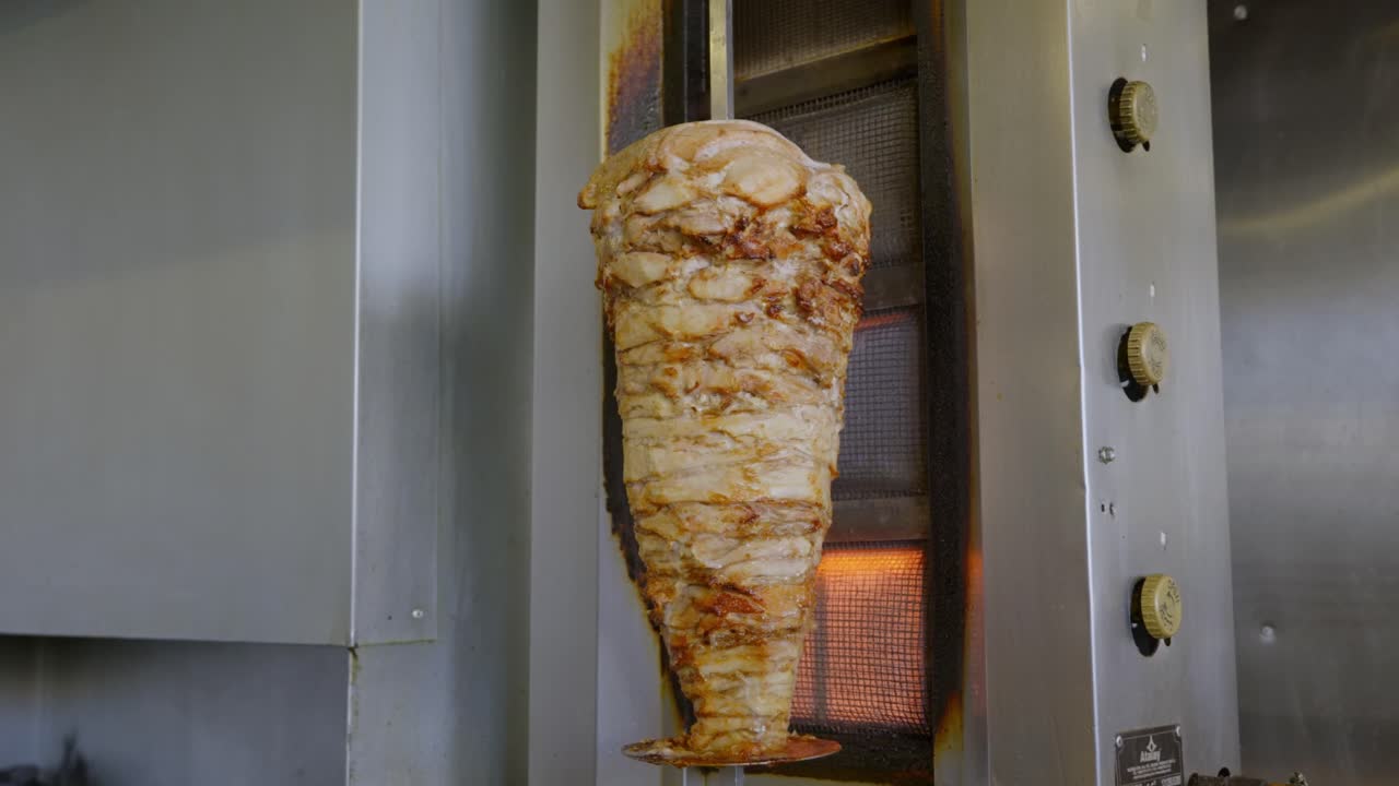 brocheta de shawarma de pollo colgada en la parrilla girando en llamas