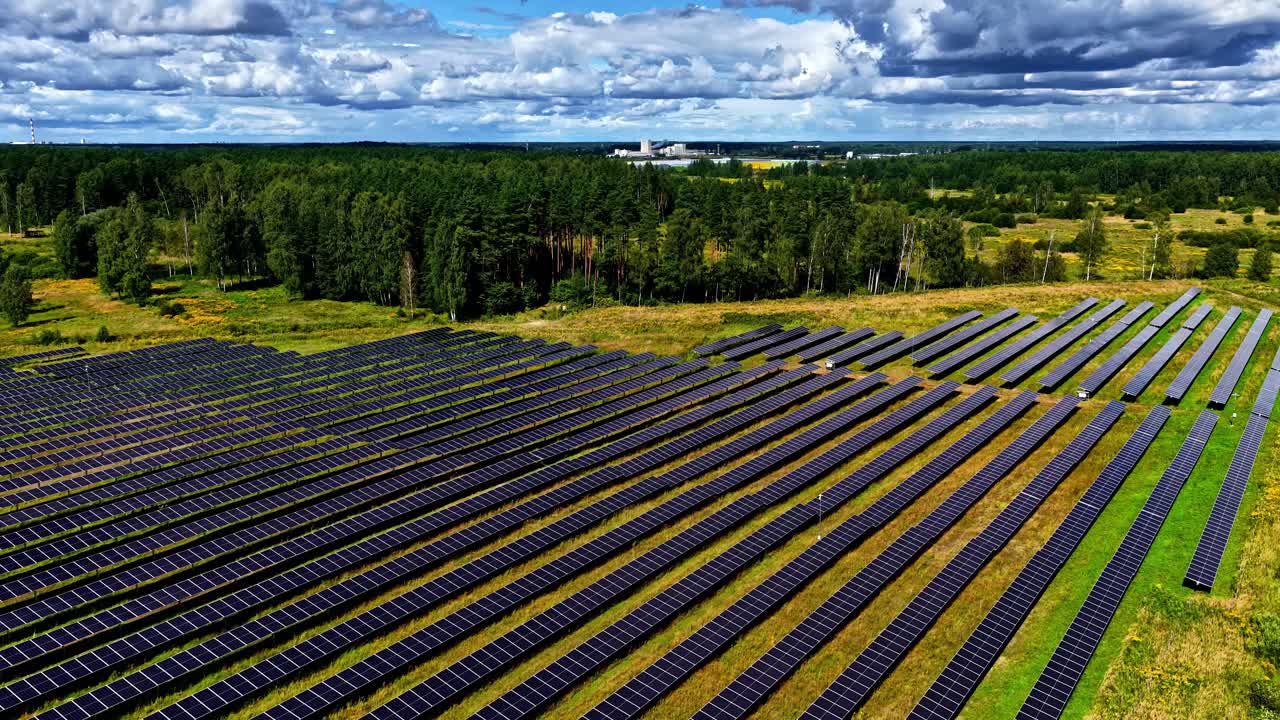 Solcellepark i et landområde med en stor fabrik i horisonten, der symboliserer energiovergangen. Fremadrettet luftfoto.