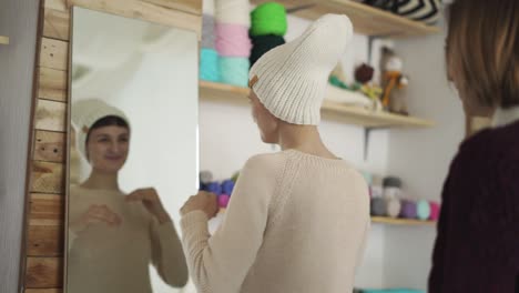 mujer sonriente vistiendo gorro de punto y mirándose en el espejo en la sala de exposición