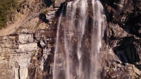 aerial drone footage raising up a picturesque waterfall with colorful rainbow reflections at fallbach in grindelwald in the swiss alps