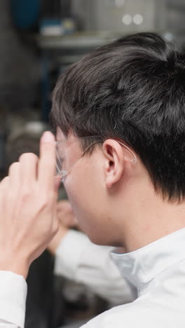 자동차 작업실에 앉아있는 실험실 엔지니어의 클로즈업, 남자는 보호 안경을 착용하고 태블릿을 들고, 여자는 기계와 조직된 장비로 둘러싸인 그녀의 앞에 있는 도구에 초점을 맞추고 있습니다.