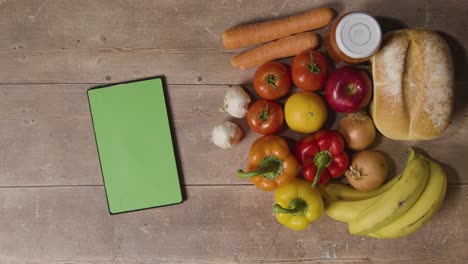 overhead studio shot of hand picking up basic fresh food items with green screen digital tablet on wooden surface 1