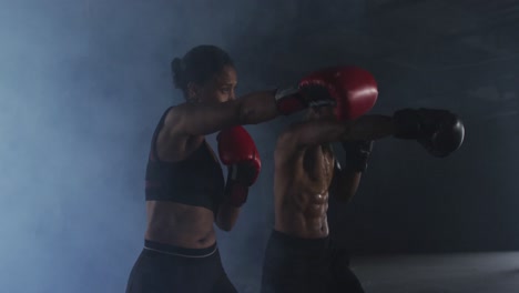 hombre y mujer afroamericanos con guantes de boxeo entrenando lanzando puñetazos en una habitación vacía