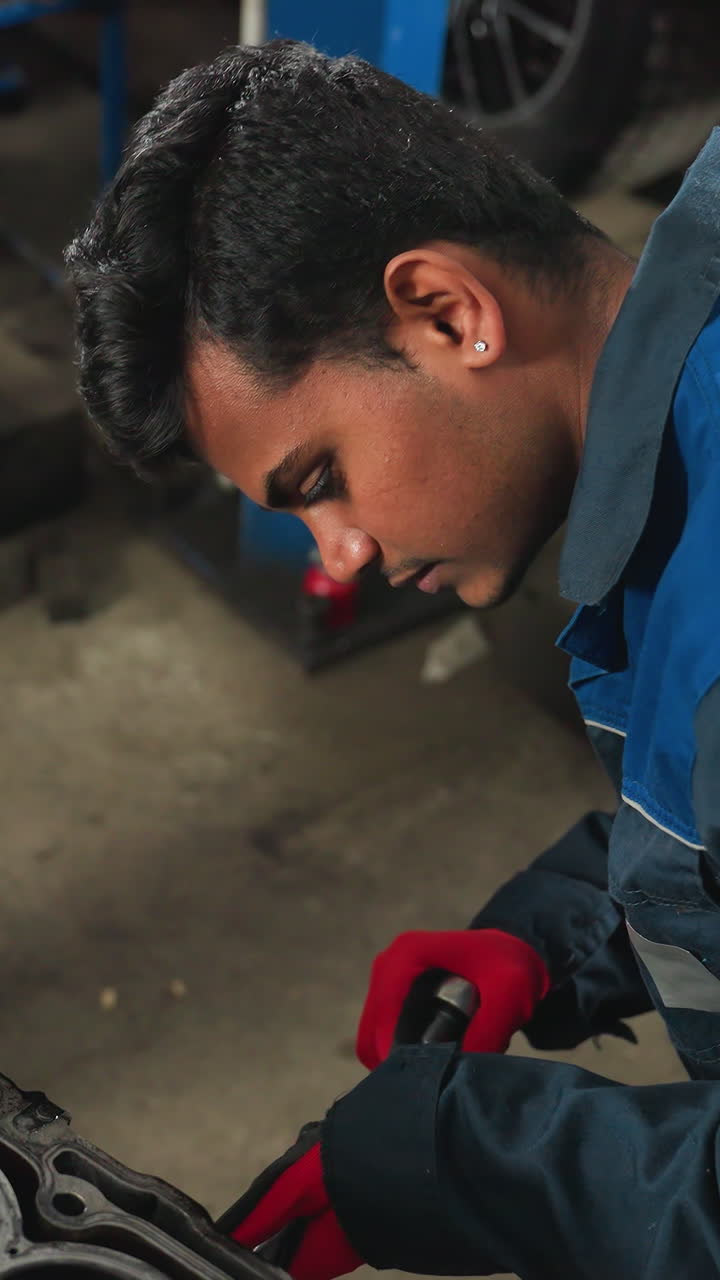 ingeniero automotriz en uniforme azul soltando una nuez doblada con guantes rojos mientras el observador en guantes blancos le muestra algo en un taller automotriz