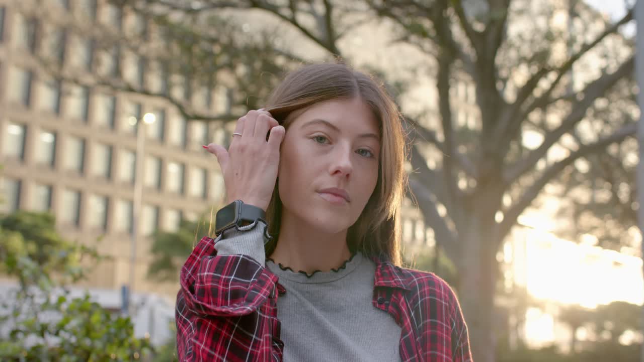 La luce del sole fa sì che una donna chiuda gli occhi, ruoti la testa sistemandosi i capelli, con uno smartwatch, in un parco.