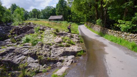 Young-boy-walking-across-rocks-in-the-Lake-District-with-a-camera-and-tripod