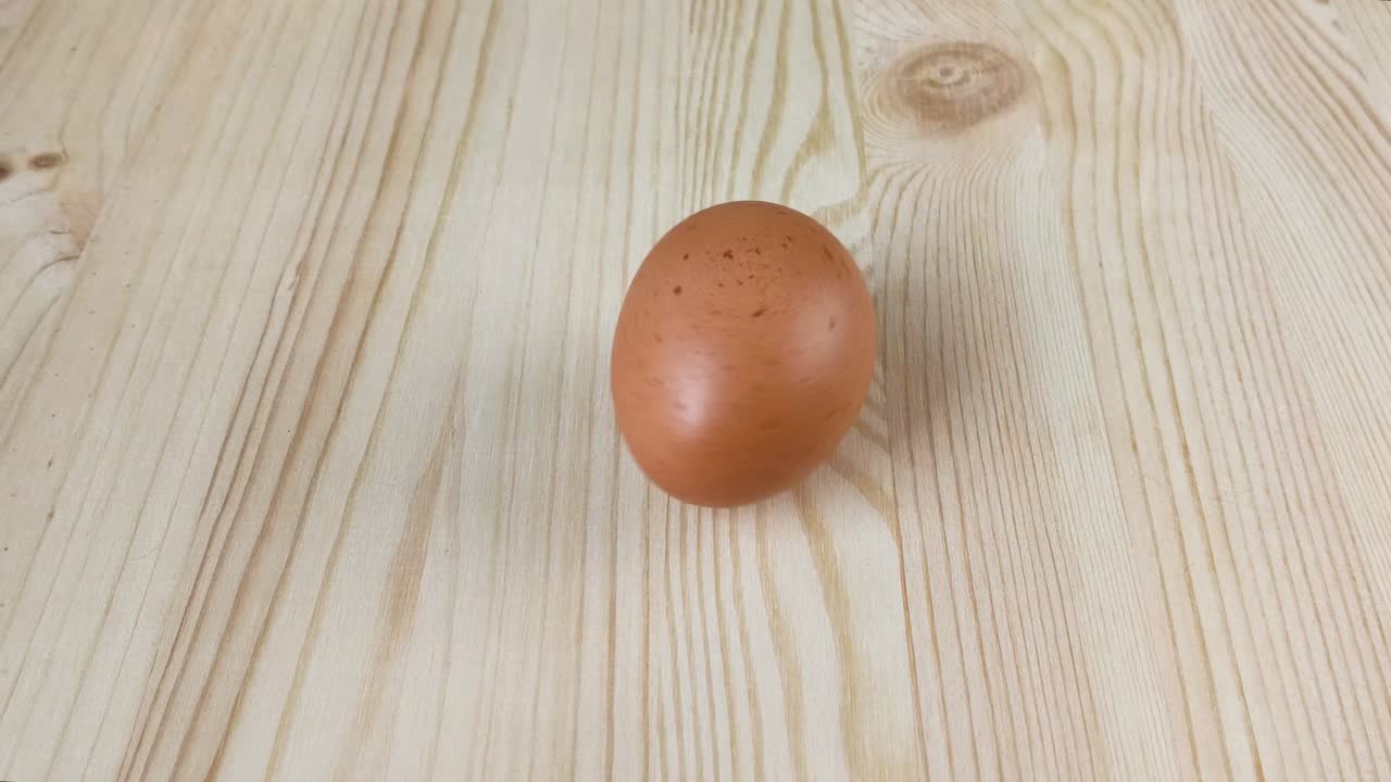 Brown chicken egg spins on wooden table