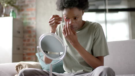 African-american-man-sitting-on-sofa,-applying-under-eye-patches-at-home,-slow-motion