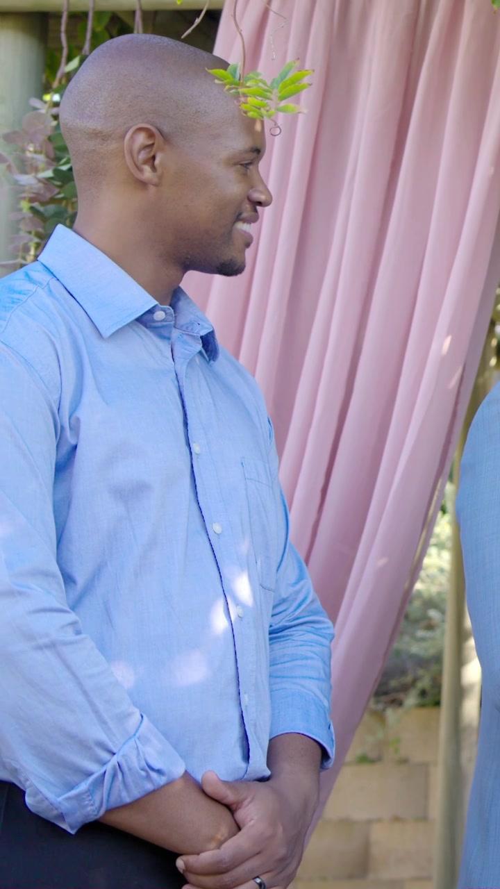 Video verticale: Uomo in camicia blu che ascolta il partner parlare e annuisce in giardino, indossando la fede nuziale.
