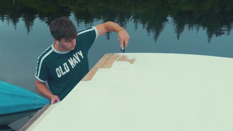 young man finishes applying primer to wooden boat roof planks