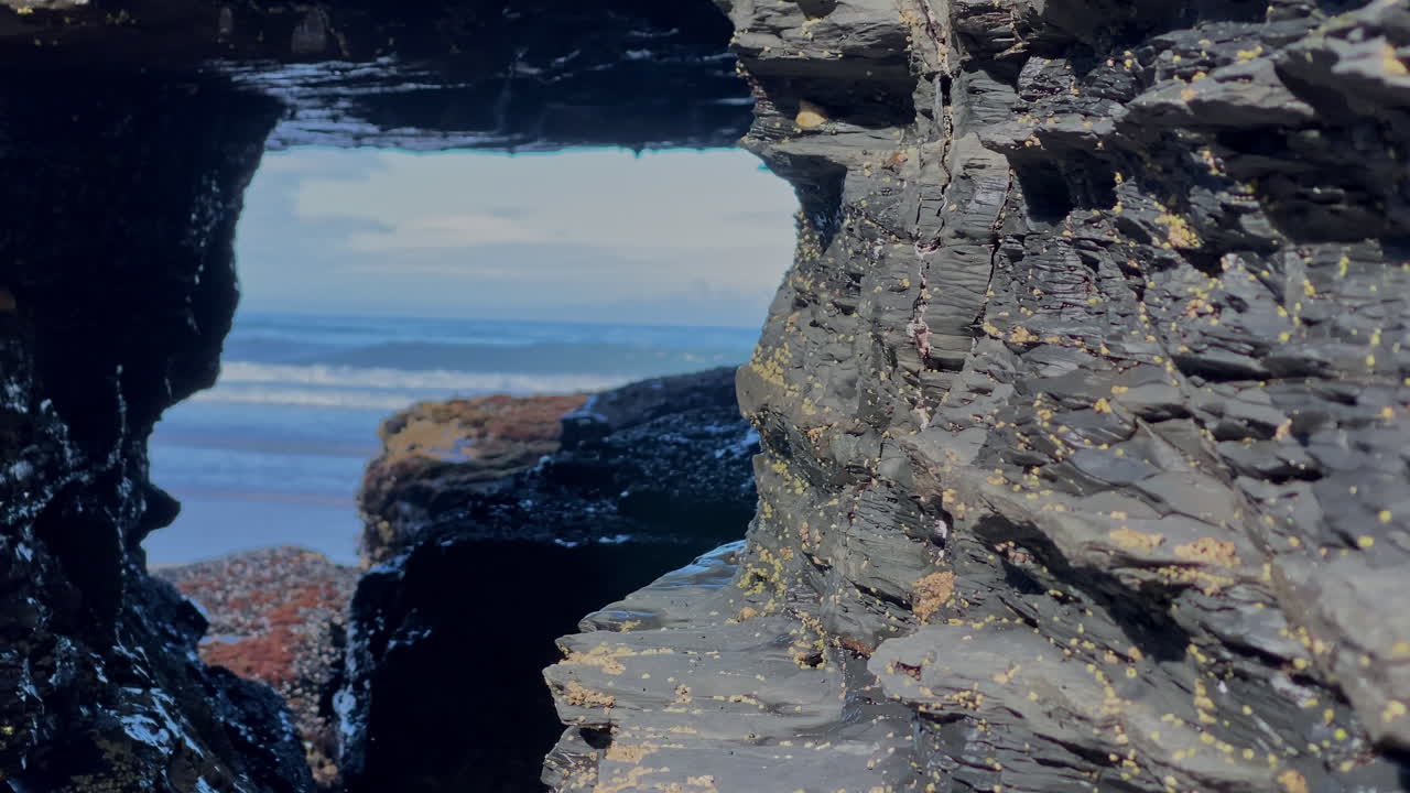 Sea reveals itself through a rocky window, waves framed by the dark stone of Sagres cliffs Black rocks crisscrossed by white mineral veins form patterns under the Atlantic light of Sagres