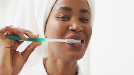 video of happy african american woman in robe brushing teeth
