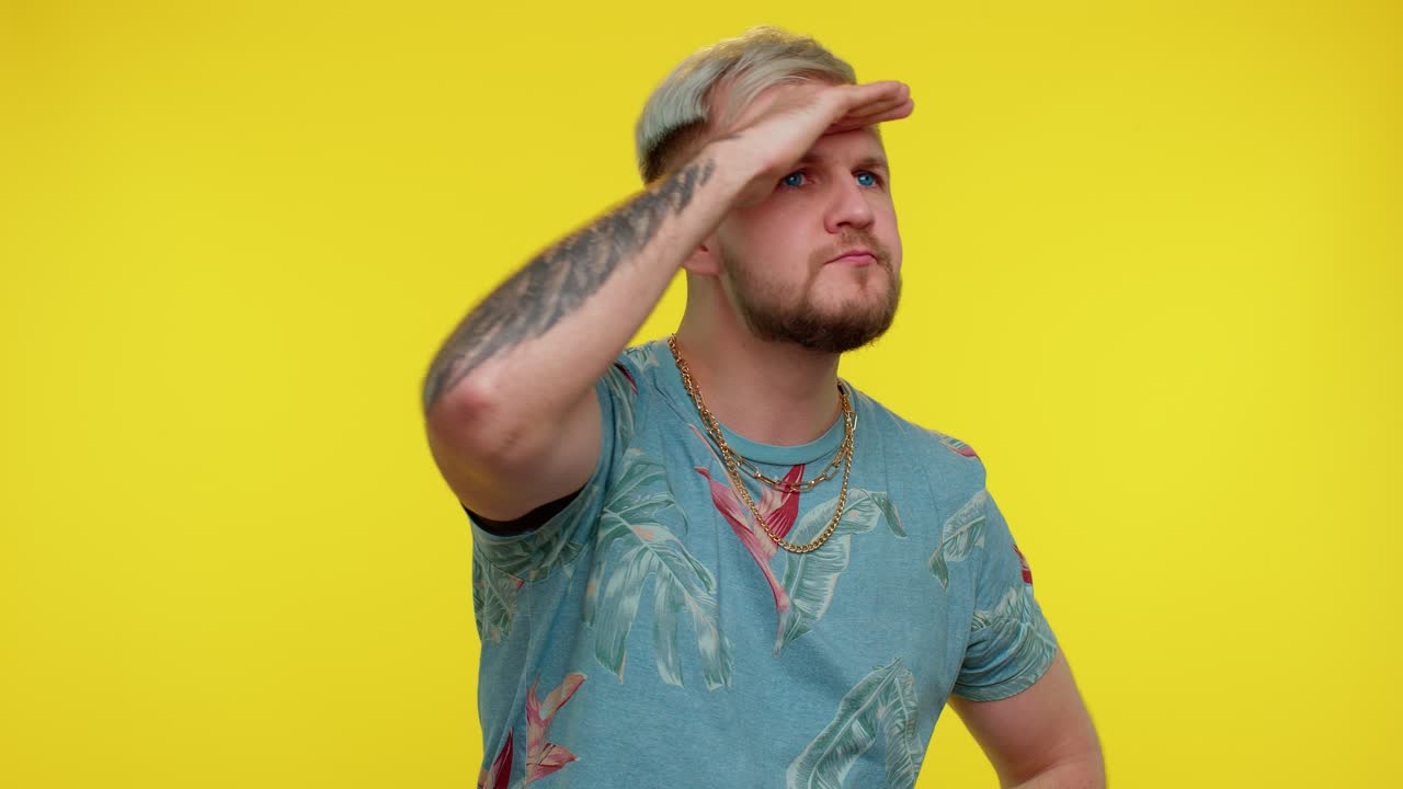 남자는 눈 위에 손을 들고, 이마를 들여다보고, 주위를 둘러보고, 누군가를 기대하고 검색합니다.