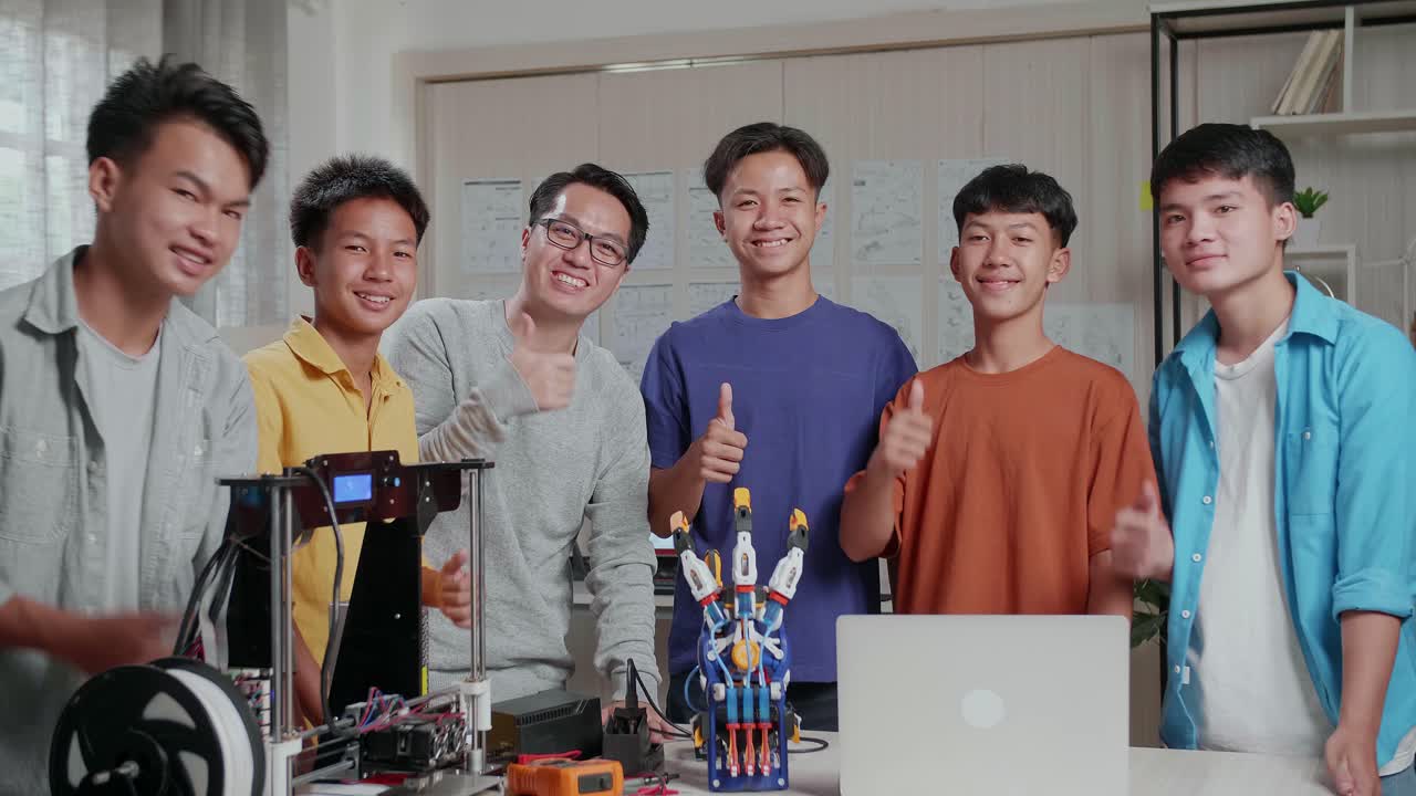 과 3d 프린팅을 가진 아시안 남자와 소년들은 학교에서 사이보그 손에 대해 논의하는 동안 미소 짓고 엄지손가락을 카메라로 제스처합니다.