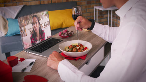 Pareja-Diversa-En-Una-Videollamada-De-Una-Cita-De-San-Valentín-Hombre-Comiendo-Comida-Con-Una-Mujer-Sonriente-En-La-Pantalla-Del-Portátil