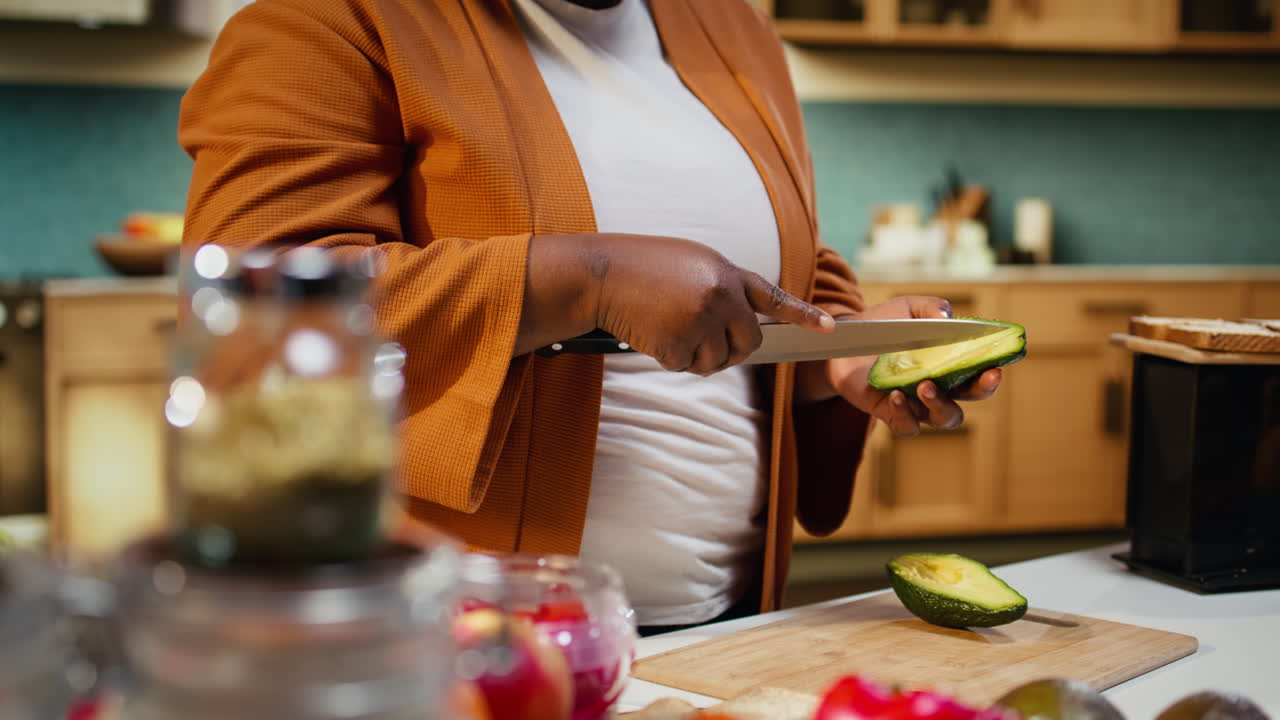 Content creator afroamericano che affetta l'avocado, processo di cucina, chef casalingo.