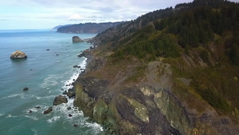 Drone-pull-back-of-Pacific-Northwest-cliffs,-forests,-and-coast,-super-wide-birds-eye-view