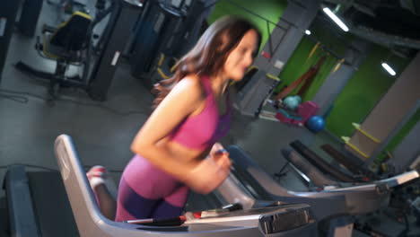 happy face of positive woman in purple sportswear is running on a treadmill in the gym. sporty smiling girl training on a racetrack inside the modern fitness centre