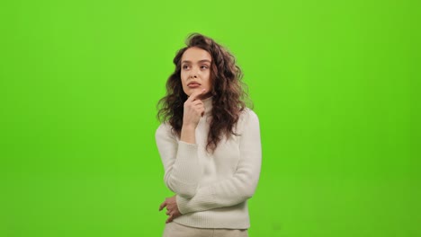 the woman is standing and looking at the camera. she is thinking and holding her hand to her chin. she is standing on a green background. green screen. 4k.