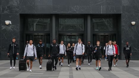 Athletes Departing Venue: A Group of Team Members Exiting the Building with Luggage and Bottles, Showcasing Unity and Purpose in Their Journey