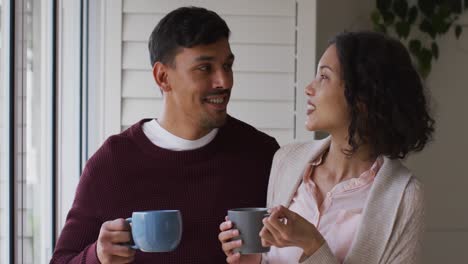 romantic hispanic couple embracing standing in window having coffee