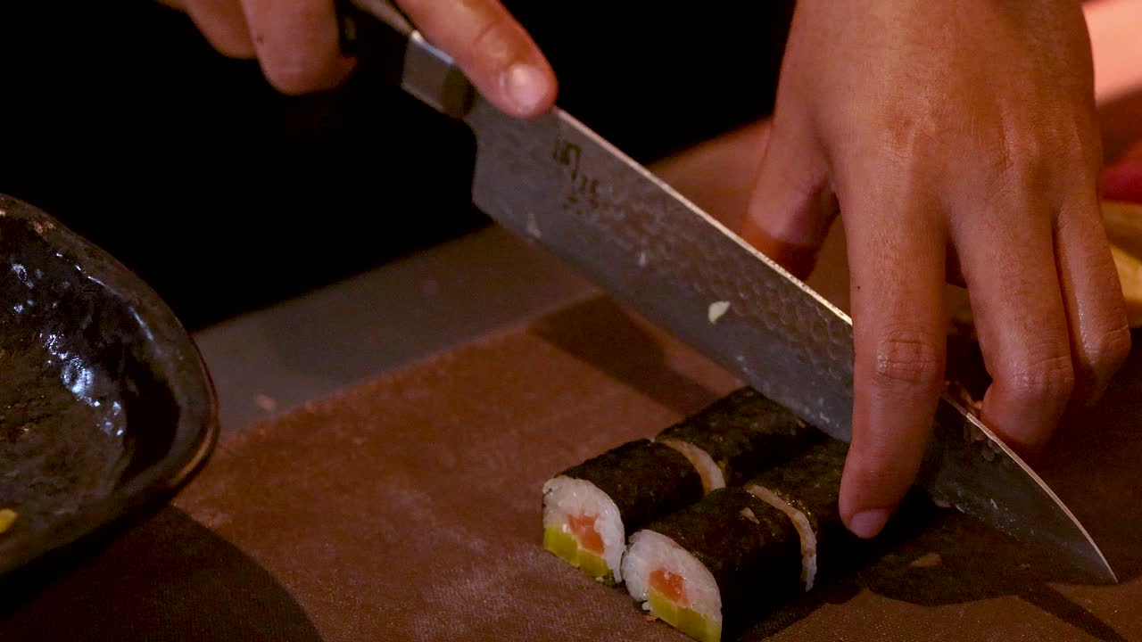 Detailní záběr kuchaře krájejícího maki rolky a aranžujícího je na pultu