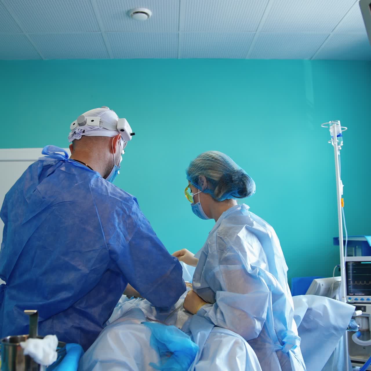 Back view of surgeon and nurse standing over the patient in surgery room. Medics perform operation for breast enlargement