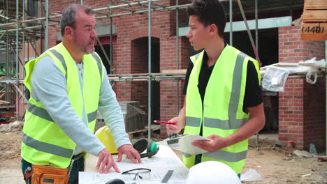 constructor en el sitio discutiendo el trabajo con el aprendiz masculino
