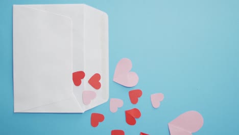 envelope with red and pink paper hearts at valentine's day on blue background