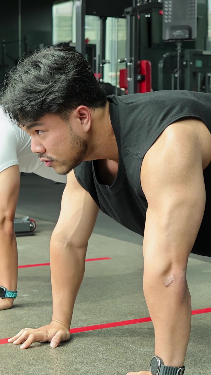 Uomo atletico in abbigliamento sportivo nero esegue mountain climbers su un pavimento di palestra in piena luce