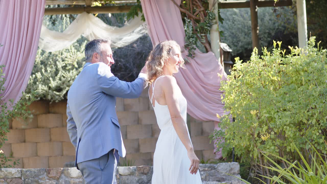 Par i formel beklædning udveksler smil, fejrer og langsomt danser på stentrappen under en pergola.
