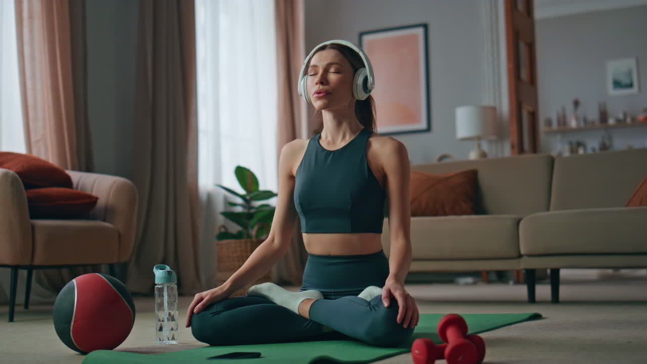 Inspired woman sitting lotus position in headphones home. Girl practicing yoga