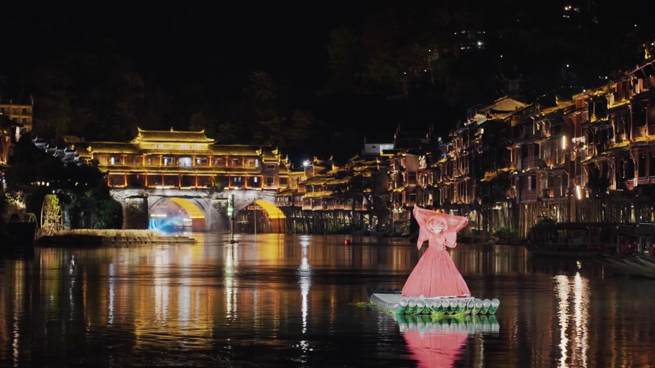 Paisagem urbana noturna de rio, ponte iluminada, lanterna flutuante. Noite serena mostra uma vila histórica à beira-rio brilhando com luzes douradas refletindo na água, com uma instalação de lanternas florais rosa flutuando.