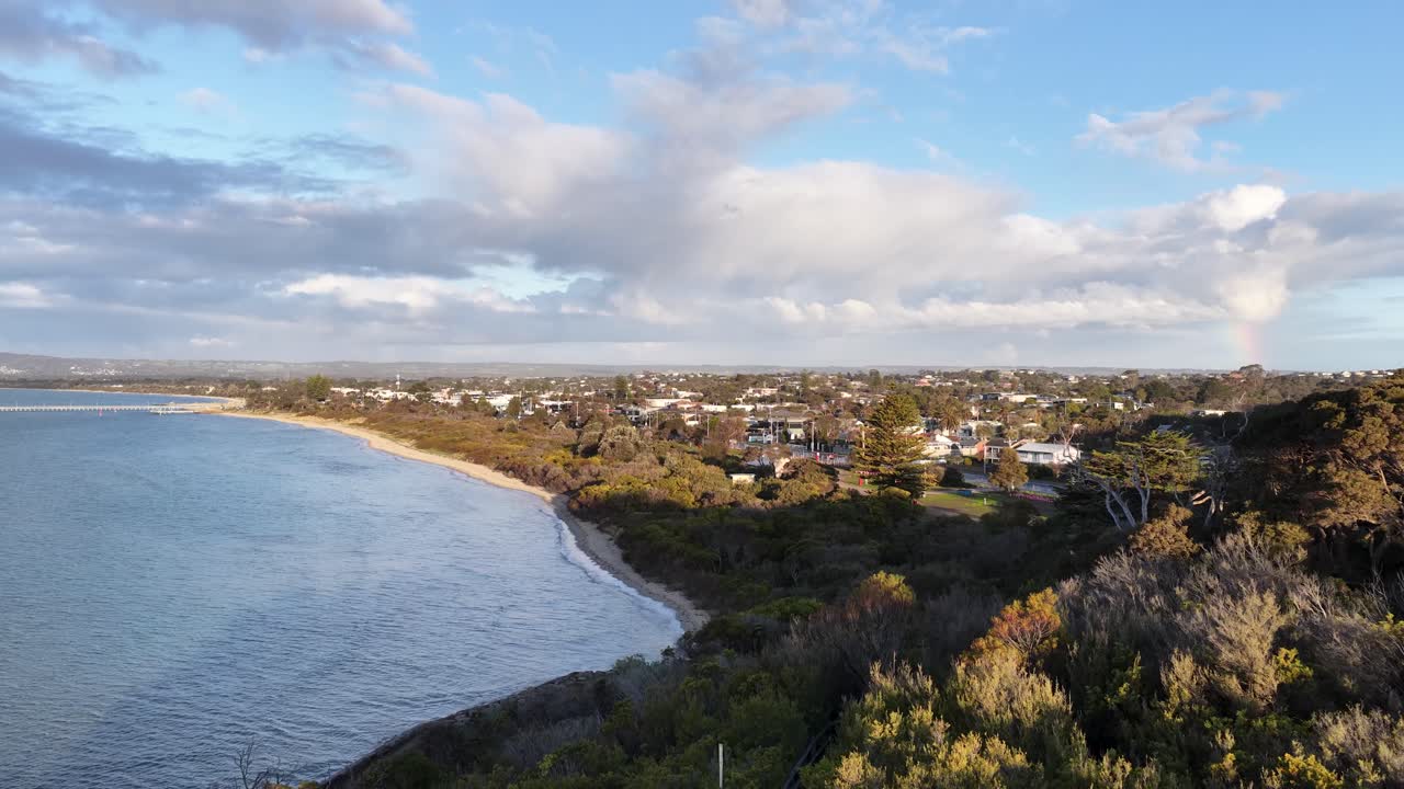 Drone glides above Rye coastline, revealing cliffs, beach, ocean, and residential area in golden light