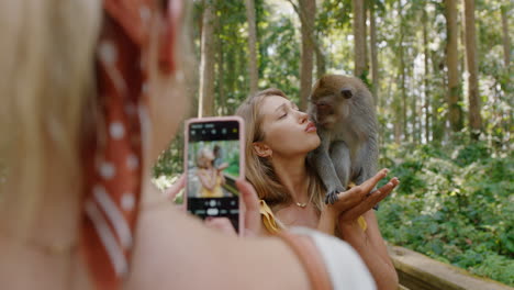 Reisefrau-Posiert-Für-Ein-Foto-Mit-Affen,-Der-Auf-Der-Schulter-Sitzt.-Beste-Freundin-Nutzt-Smartphone-Und-Fotografiert-Verspielte-Affen,-Die-Ihr-Abenteuer-In-Der-Tierwelt-Teilen