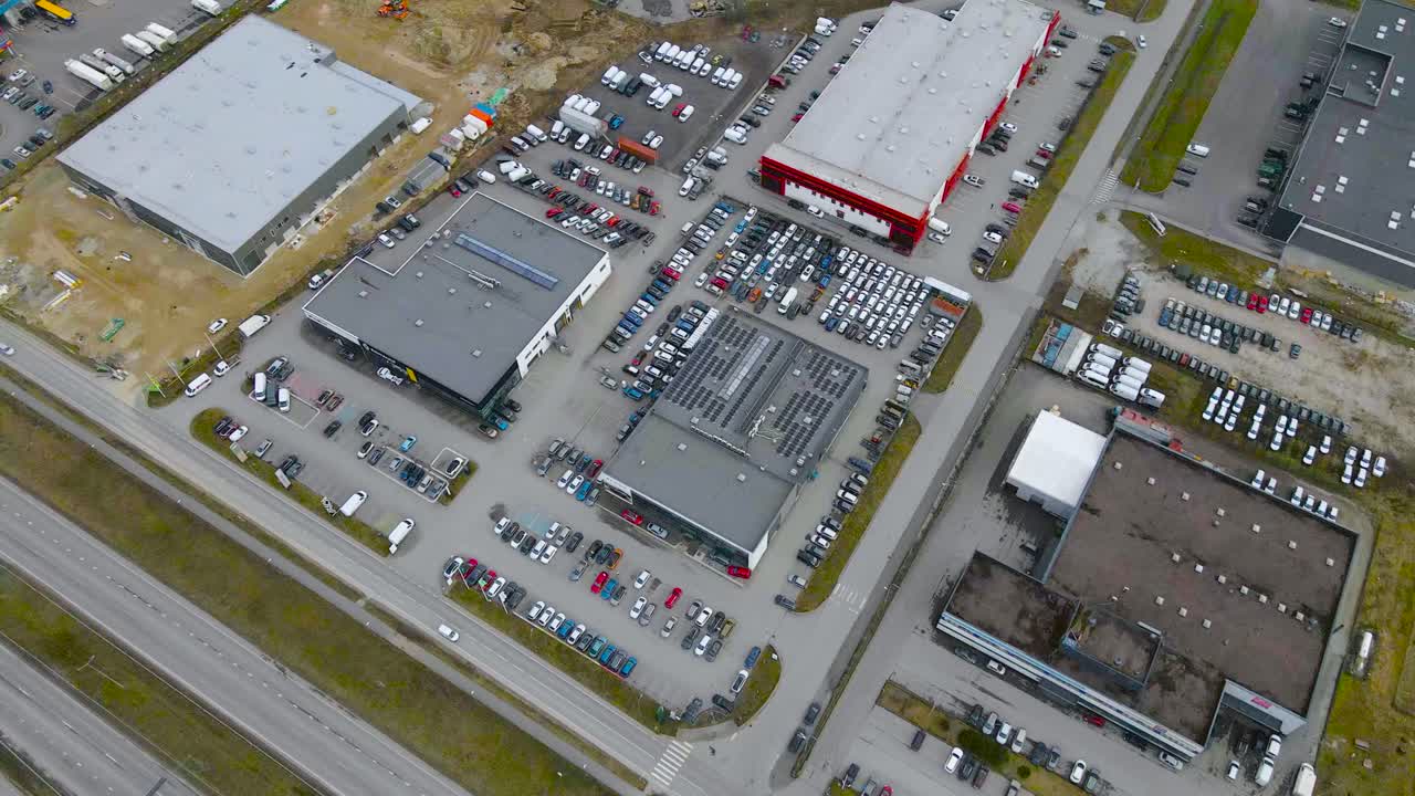 Aerial drone footage view of manufacturing warehouses and buildings in Laagri Estonia near Tallinn Pärnu highway during a cloudy spring or autumn day. Cars, vehicles and trucks drive on the road below