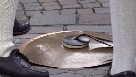 three pairs of feet clad in traditional shoes and socks stand around cymbals placed on the ground, capturing a moment of anticipation before the music starts.