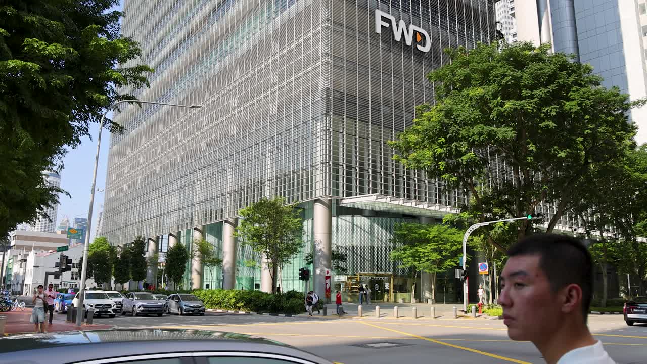 Man crosses street with traffic near glass office tower, daylight, wide shot, urban Singapore