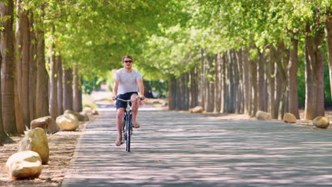 young white man riding bike on a tree lined road