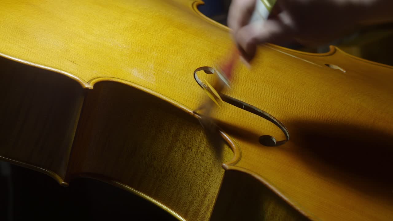 Close up of a luthier's meticulous varnishing work on a cello f hole, showcasing the precision and artistry involved in crafting musical instruments with traditional manual methods